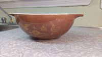 Side profile of largest brown Pyrex Early American Cinderella bowl showing gold rooster and kitchen motifs.