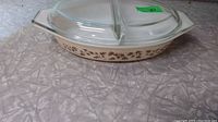 Full side view of the Pyrex divided casserole dish with clear lid in place on textured surface.