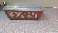 Side view of rectangular brown Pyrex refrigerator dish with white Early American decals showing eagle and symbols.