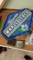 Photo showing Toronto Maple Leafs electric sign and two Budweiser belt buckles on a table