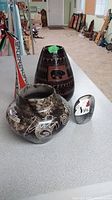 Photo showing three of the four Indigenous vases on a table including large dark vase with bear motif and smaller marbled vase with white motifs.