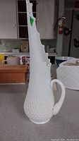 Side view of tall milk white glass vase with hobnail texture and swung drip top edge, showing handle and irregular rim shape.