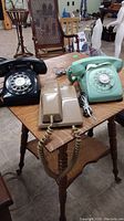 Three vintage rotary dial telephones on a wooden table including black, light green, and beige models.