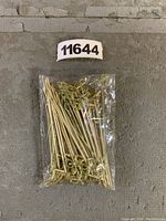 Plastic bag holding about 50 natural bamboo cocktail picks with knotted ends lying on concrete floor.