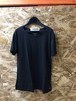 Black short-sleeve T-shirt hanging on black plastic hanger against wood background