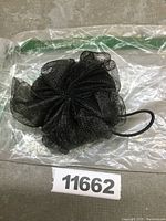 Top view of black mesh bath pouf in sealed bag.