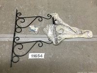 Photo showing four black metal plant hanging bracket hooks arranged on a floor with mounting hardware visible.