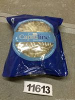 Front of blue bag packaging with clear window showing empty gelatin capsules inside. Brand Capsuline, since 2002.