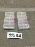 Two clear plastic pill boxes with 10 sections each side-by-side, sealed in plastic wrapping with a pink press buckle visible on the side.