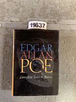 Front cover of the hardcover book 'Edgar Allan Poe Complete Tales & Poems' with title in blue, red, yellow text over dark ghostly background.