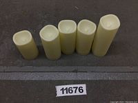 Five ivory flameless candles of varying height, unlit, arranged in a row on a dark surface.