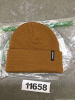 Brown knit toque hat with folded cuff and FURTALK tag displayed flat on plastic packaging.
