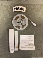 Photo of the LED strip light roll, USB motion sensor switch, waterproof battery box, and instruction manual laid out on a surface.