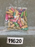 Clear plastic bag containing multiple small cone incense pieces in various colors shown on a neutral surface with lot number.
