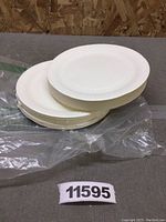 Stack of white paper plates resting on plastic wrapping on a floor with wooden wall background