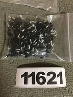Clear plastic bag filled with multiple small black metal screws with hooks, laid on a concrete floor with lot number 11621 visible.