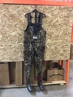 Full front view of the chest waders hanging, showing camouflage pattern, adjustable straps and attached boots