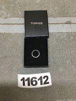 Titanium ring in a black TIGRADE box, top view showing ring centered inside box with lid open.