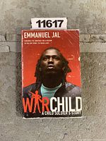 Front cover of 'War Child: A Child Soldier's Story' paperback showing author Emmanuel Jal with a red background and worn edges.