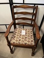 Front view of antique wooden armchair with floral cushioned seat and three horizontal back slats.