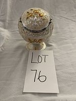 Front view of round orb shaped antique metal ashtray on pedestal base with engraved floral and gold-tone decoration.