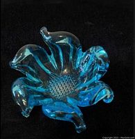 Top-down view of bright blue glass dish shaped like a flower with curling petal edges and textured center, placed on black background.