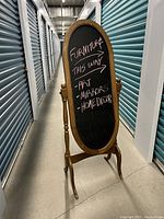 Full view of the oval wooden chalkboard mirror stand showing the frame, stand legs, and chalk writing on the board.