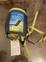 Photo of Tesco Micro-Lite mummy sleeping bag compressed into a green and black compression sack with attached straps, placed on wooden floor with lot number 117.