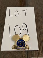 Gold Disneyland 50th Anniversary pin shaped as Mickey Mouse head with blue circle and '50' and 'Disneyland' text.