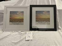 Two 12x12 square picture frames on a white cloth, one white and one black, both with mats and sealed in plastic wrap.
