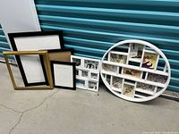 Group of different frames arranged on floor including large round white collage frame and various black, gold, and white single frames