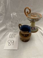 Full lot with crystal basket, ceramic candle holder, and bronze pitcher shown together on white fabric background.