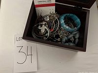 Open wooden jewelry box filled with various costume jewelry items such as bangles, earrings, necklaces, and bracelets