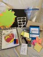 Overview of various office supplies including colored paper cutouts, markers, black adhesive labels, brown envelopes, and sticky notes