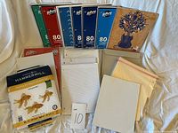 Full view of various office supplies including lined notebooks, sketchbook, printer paper, file folders, graph paper sheets, and note pads