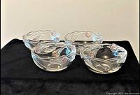 Four clear glass bowls on a black fabric surface, each decorated with a pink lily embedded in the glass.