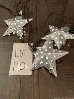 Aluminium star-shaped lights with star cut-out pattern on brown wire, spread out on floor showing detail and plug.
