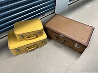 Three vintage suitcases: two yellow stacked on top of each other and one large brown suitcase beside them