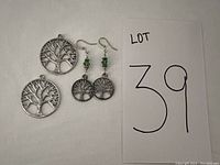 Photo of two round Tree of Life pendants and a pair of matching earrings with green beads on a white background along with lot number.