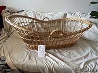 Side view of vintage wicker baby bassinet showing overall structure and handle detail.