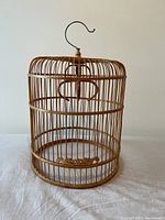 Full view of the wooden birdcage showing circular vertical rod construction with hanging hook on top, open bottom, and sliding door feature.