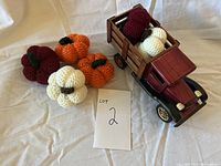 Wooden pickup truck with 6 crochet pumpkins of multiple colors around it on a light fabric background.