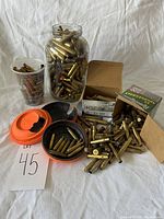 Wide shot of multiple containers filled with empty brass ammunition shells along with cardboard boxes and clay shooting targets.