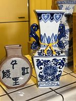Close-up of blue and white hexagonal vase with handles and brown circular vase with calligraphy in front