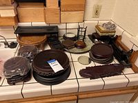 Photo of multiple Asian-style wooden display stands on a tiled counter, showing various shapes and finishes.