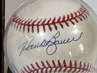 Close-up of the Hank Bauer autograph on the baseball inside the clear plastic case showing the signature in blue ink.