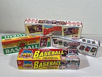 Four unopened sealed boxes of 1991 baseball card sets and a baseball puzzle box, showing the front packaging with colors and branding for Topps, Donruss, and Bowman.