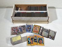 Large cardboard box filled with baseball cards in protective plastic sleeves organized in rows inside the box and a small selection of cards displayed in front.