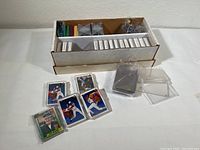 Photo of a cardboard box with rows of baseball cards and protective sleeves, plus several cards and holders displayed outside the box