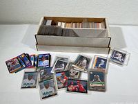 Photo of box filled with assorted baseball cards with some cards displayed in front, showing both sleeved and unsleeved cards.